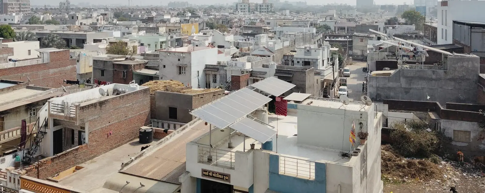 Rooftop solar panels installed on a residential home in a dense Indian neighbourhood, city skyline in the background